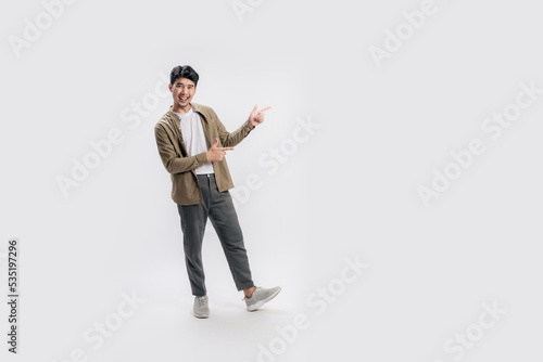 Full length of a handsome asian man pointing out to present something, the smile on his face, his hand gesture and the casual outfit are perfect for the suggestion to copy space.