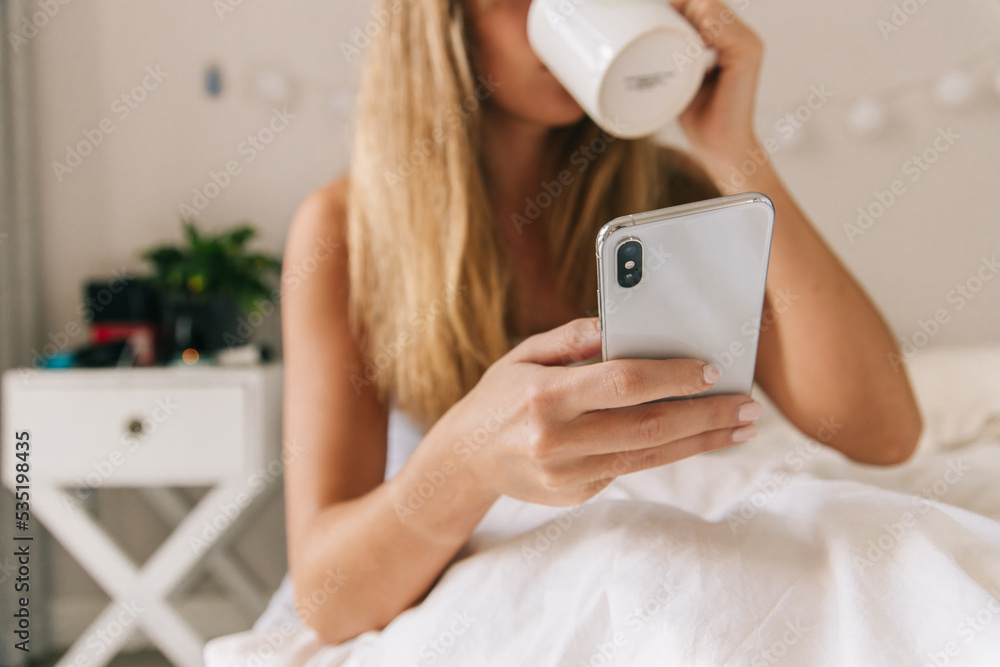 Happy woman having coffee and using phone in bed Happy woman having coffee and using phone in bed