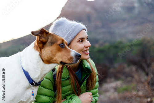 Portrait of smiling female caucasian hiker in winter clothes resting on a rock with her dog