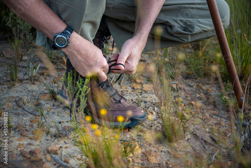 Mature male hiker tying shoelace on his hiking boot. Tourist is getting ready for hike at trekking trail