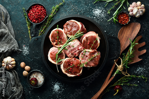 Meat. Raw Meat Veal medallions wrapped in bacon. Laid out in a pan, ready to cook. On a black concrete background. Top view.