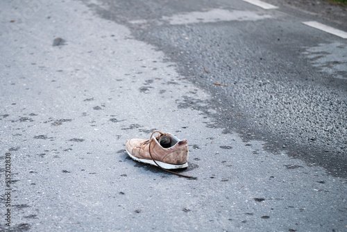 Brown sneaker on an asphalt road. Shoes on the roadway. Consequences of the accident.