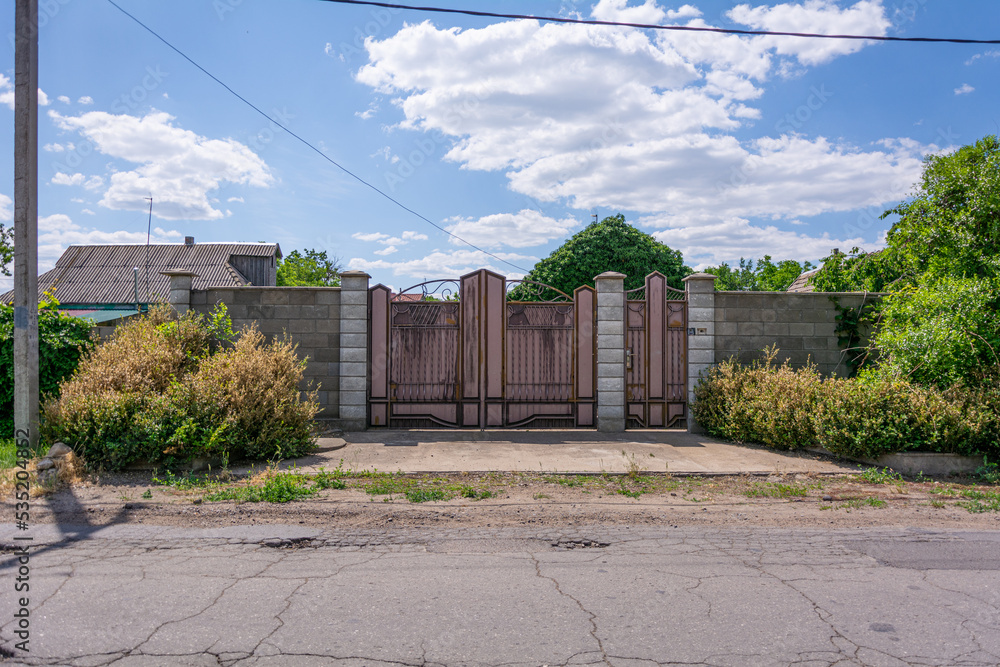 Fence of a private house. View from the street on fence with patterned iron gates encloses a private house in Transnistrian village