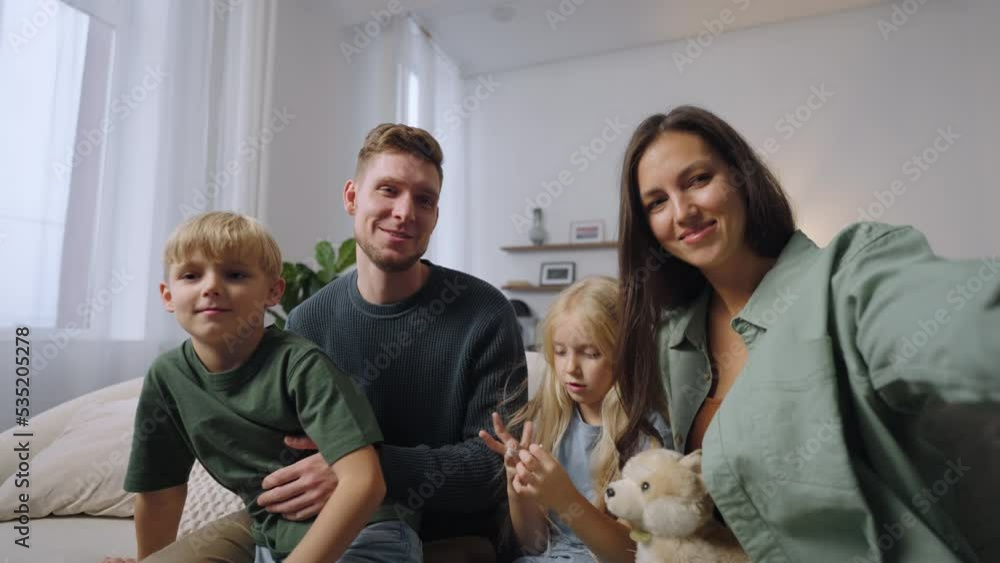 A man and a woman with two children look directly into the camera and smile talking greeting the viewer. Remote communication with friends and relatives. Family Video Blog A man and a woman with two children look directly into the camera and smile talking greeting the viewer. Remote communication with friends and relatives. Family Video Blog