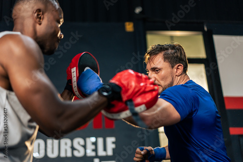 Caucasian man wear boxing gloves punching ahead with African trainer. 