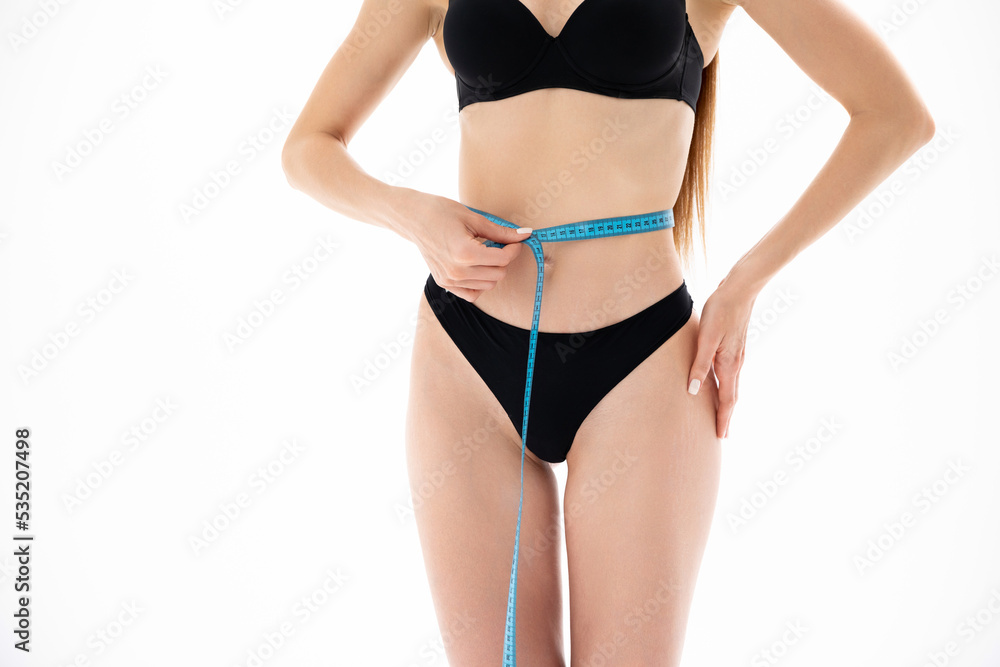 A slender girl in black lingerie measures her waist with a tape measure