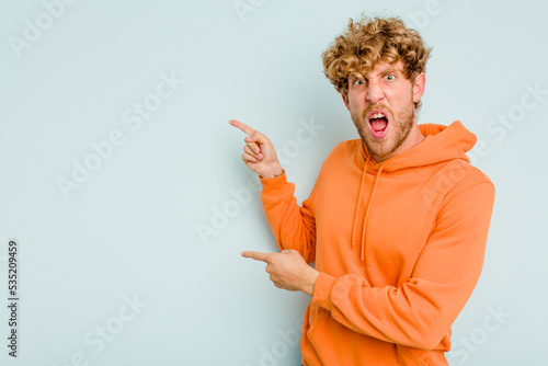 Young caucasian man isolated on blue background pointing with forefingers to a copy space, expressing excitement and desire.