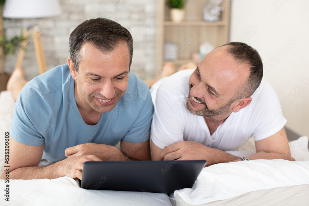 happy gay couple with tablet computer on bed at home happy gay couple with tablet computer on bed at home