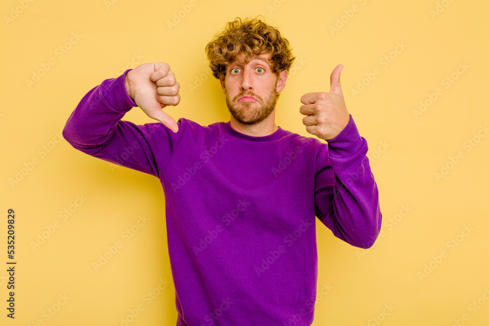 Young caucasian man isolated on yellow background showing thumbs up and thumbs down, difficult choose concept Young caucasian man isolated on yellow background showing thumbs up and thumbs down, difficult choose concept