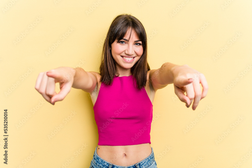 Young caucasian woman isolated on yellow background cheerful smiles pointing to front.