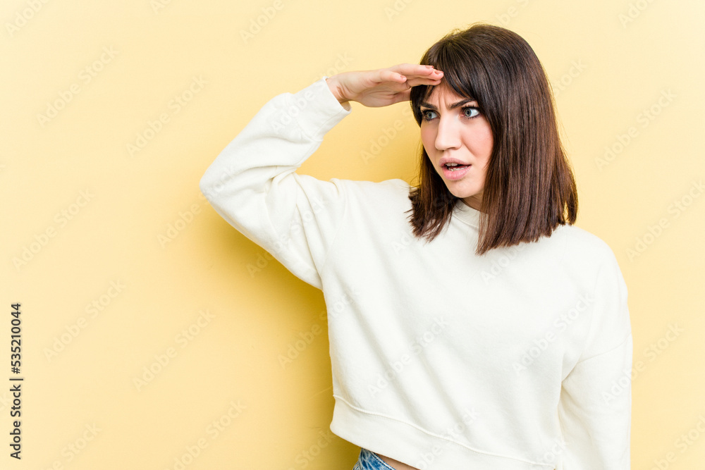 Young caucasian woman isolated on yellow background looking far away keeping hand on forehead. Young caucasian woman isolated on yellow background looking far away keeping hand on forehead.