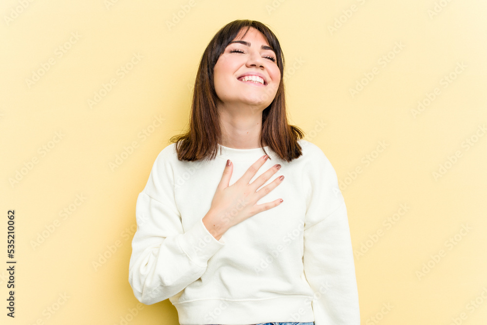 Young caucasian woman isolated on yellow background laughs out loudly keeping hand on chest. Young caucasian woman isolated on yellow background laughs out loudly keeping hand on chest.
