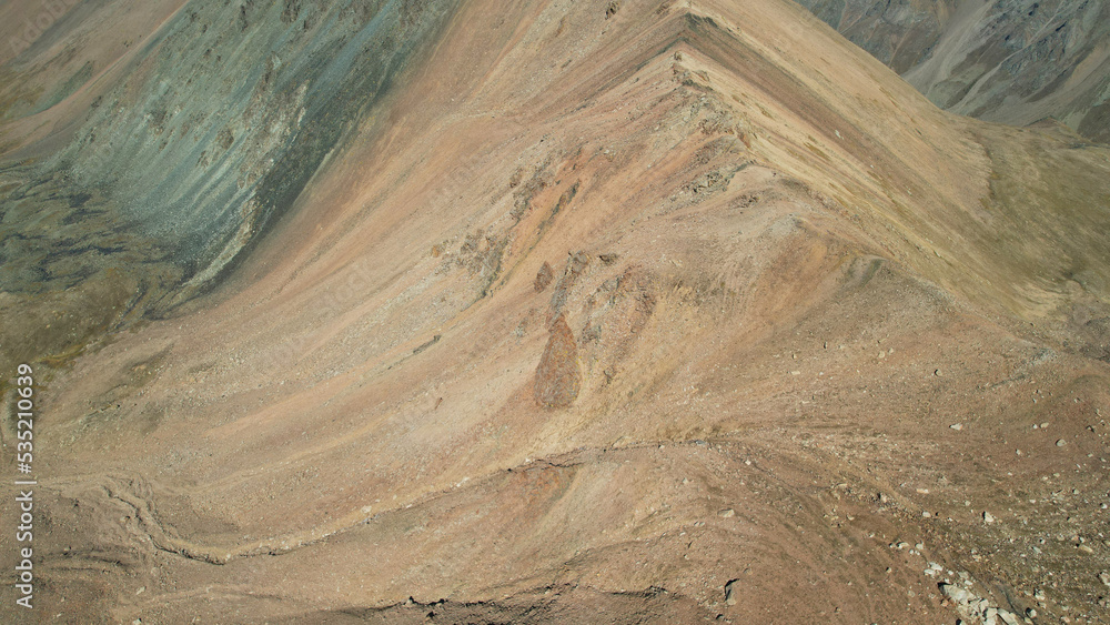 A mountain pass with a steep descent and rocks. Rocky terrain. Traces of falling rocks and a melting glacier are visible. Cliff break. There is snow in places. Top view from a drone. Kazakhstan