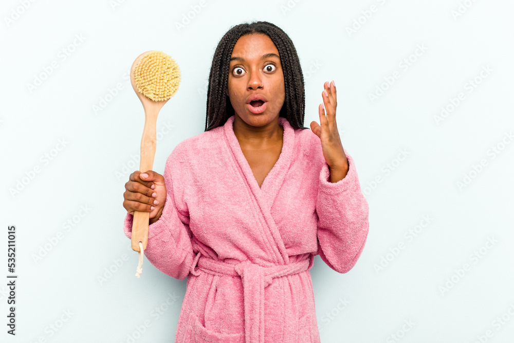 Young African American woman holding a bathtub brush isolated on blue background surprised and shocked. Young African American woman holding a bathtub brush isolated on blue background surprised and shocked.