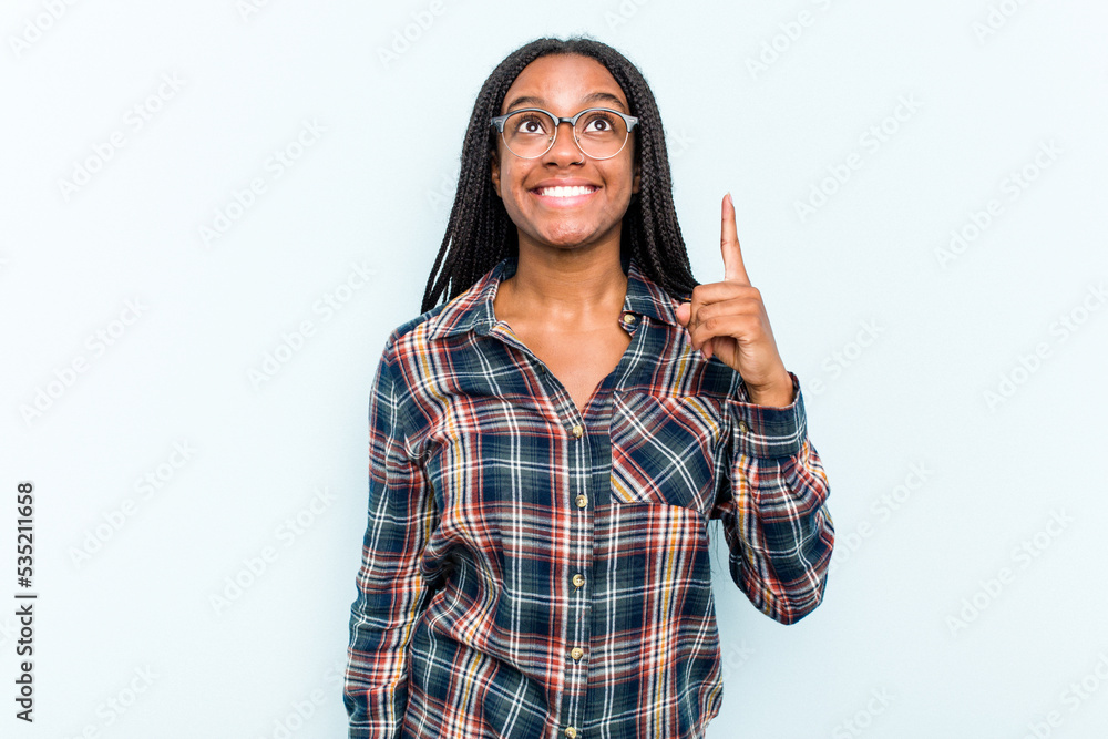 Young African American woman with braids hair isolated on blue background indicates with both fore fingers up showing a blank space. Young African American woman with braids hair isolated on blue background indicates with both fore fingers up showing a blank space.
