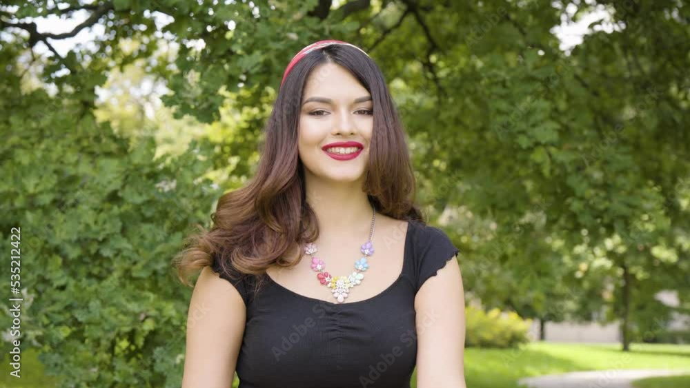 A young beautiful Caucasian woman smiles at the camera in a park on a sunny day A young beautiful Caucasian woman smiles at the camera in a park on a sunny day