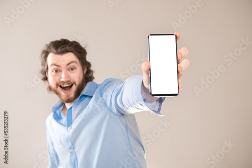 Handsome young man showing blank cellphone screen isolated on gray background with copy space photo