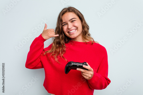 Young caucasian gamer woman holding a game controller isolated on blue background showing a mobile phone call gesture with fingers.