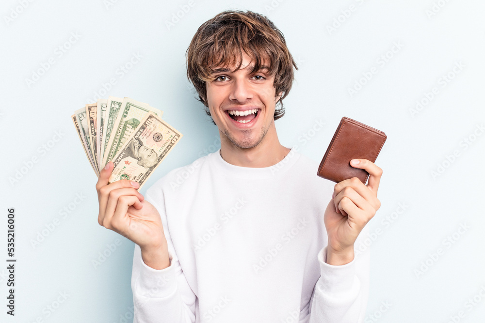 Young caucasian man holding wallet and banknotes isolated on blue background Young caucasian man holding wallet and banknotes isolated on blue background
