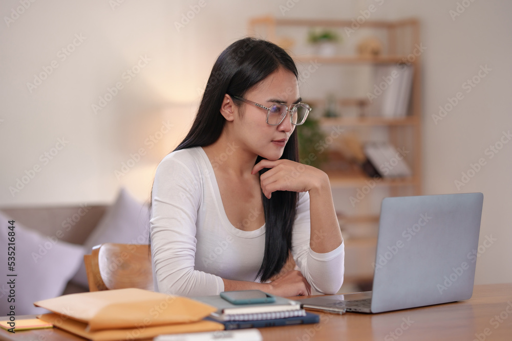 Beautiful Asian woman sitting intently working on a laptop computer at home. Beautiful Asian woman sitting intently working on a laptop computer at home.