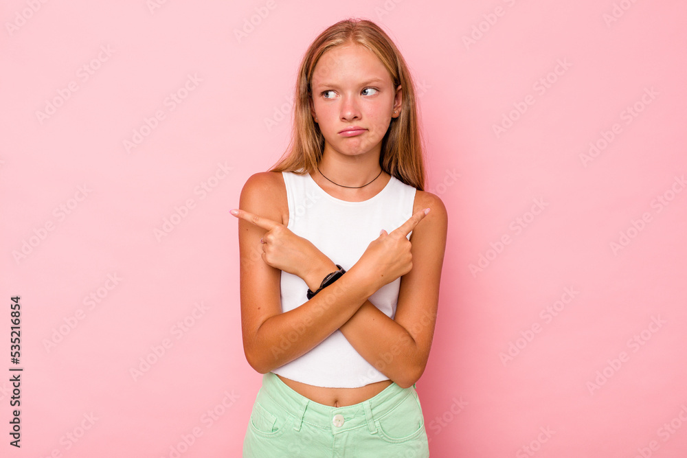 Fototapeta premium Caucasian teen girl isolated on pink background points sideways, is trying to choose between two options.