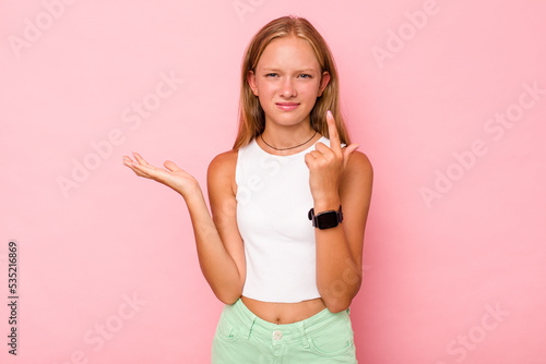 Caucasian teen girl isolated on pink background holding and showing a product on hand. © Asier