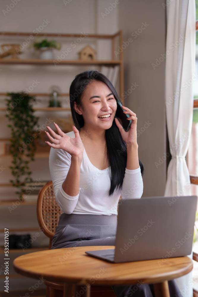 Asian woman sitting at home working on her laptop and talks on the phone comfortably and refreshed on a new day. Asian woman sitting at home working on her laptop and talks on the phone comfortably and refreshed on a new day.
