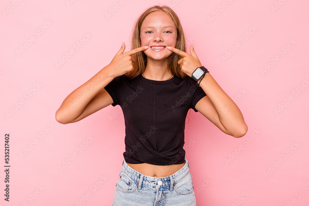 Caucasian teen girl isolated on pink background smiles, pointing fingers at mouth. Caucasian teen girl isolated on pink background smiles, pointing fingers at mouth.