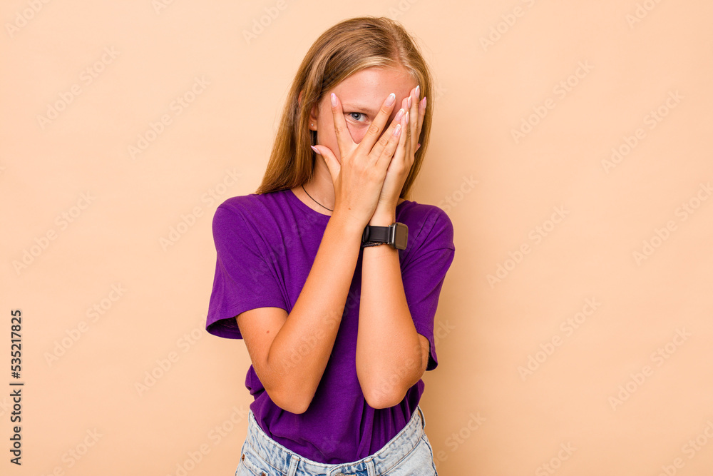 Caucasian teen girl isolated on beige background blink through fingers frightened and nervous. Caucasian teen girl isolated on beige background blink through fingers frightened and nervous.