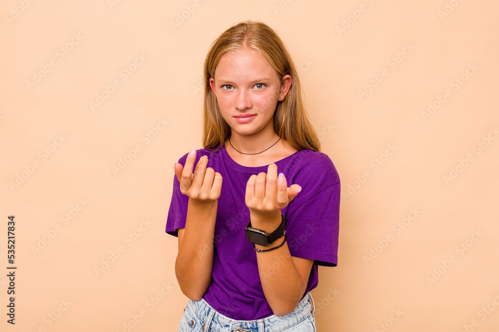 Caucasian teen girl isolated on beige background pointing with finger at you as if inviting come closer. Caucasian teen girl isolated on beige background pointing with finger at you as if inviting come closer.