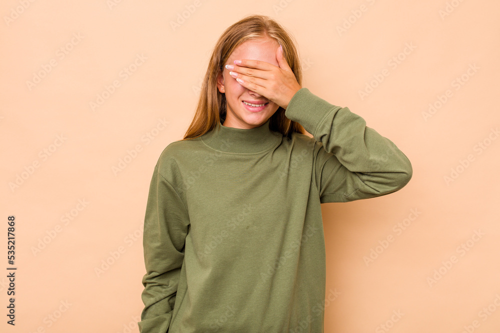 Caucasian teen girl isolated on beige background covers eyes with hands, smiles broadly waiting for a surprise. Caucasian teen girl isolated on beige background covers eyes with hands, smiles broadly waiting for a surprise.
