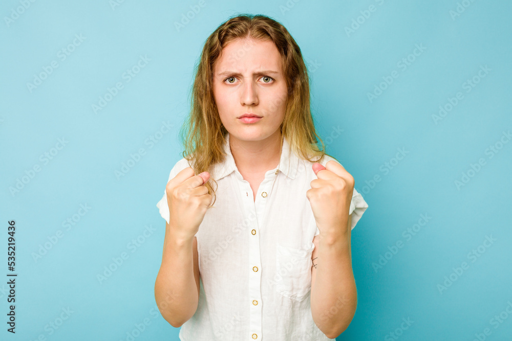 Young caucasian woman isolated on blue background showing fist to camera, aggressive facial expression. Young caucasian woman isolated on blue background showing fist to camera, aggressive facial expression.