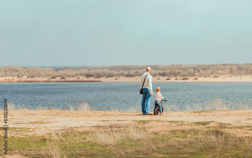 People on a beach. Father and child from behind standing on the riverbank and looking into the distance at the river