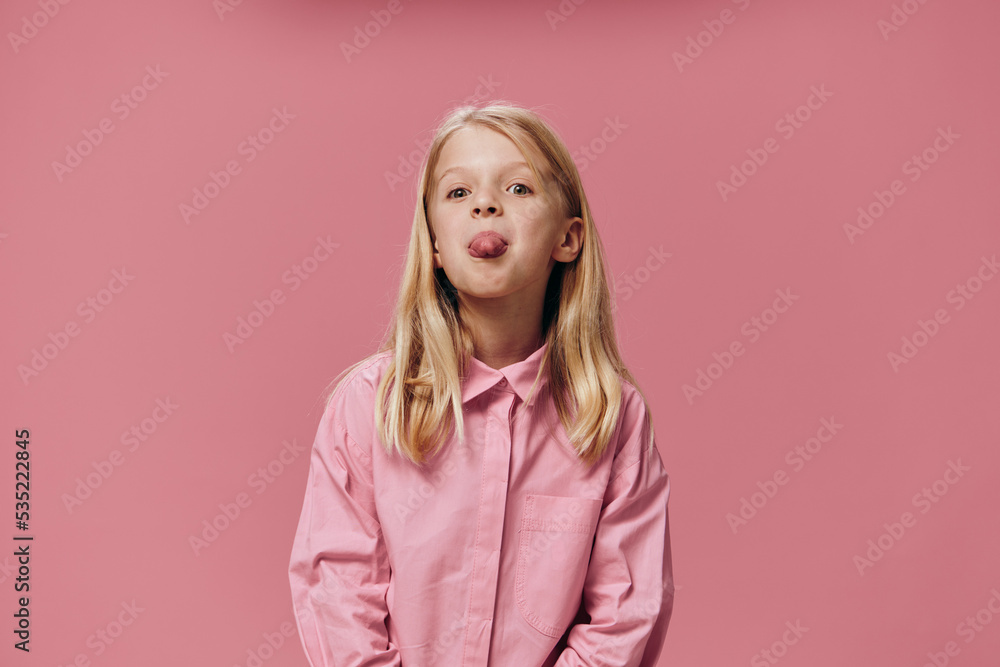 a beautiful, small, funny girl stands in a pink shirt on a pink background and shows her tongue at the camera a beautiful, small, funny girl stands in a pink shirt on a pink background and shows her tongue at the camera