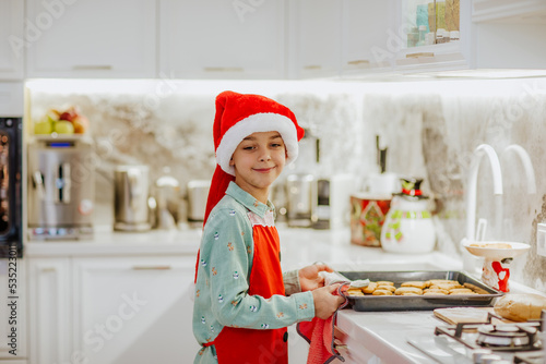 Boy in red Santa's hat is cooking Christmas cookies on white home kitchen