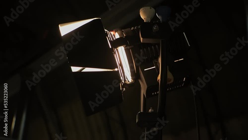 Halogen source of constant lighting equipment. Lightweight fresnel spotlight searchlight is on set during shooting of film. Lamphead. Dark stage, scene. Movie cinema production. Gafer's work on-set