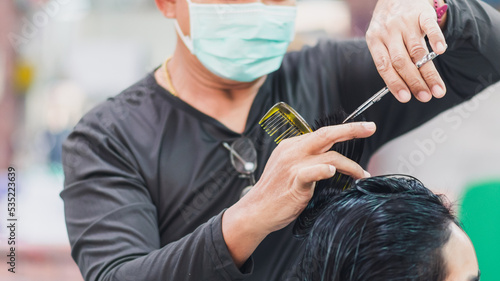 professional man hairdresser wearing face mask holding scissors and haircutting client woman indoor salon, man make business hair care has tool haircut to service haircut to customer, selective focus