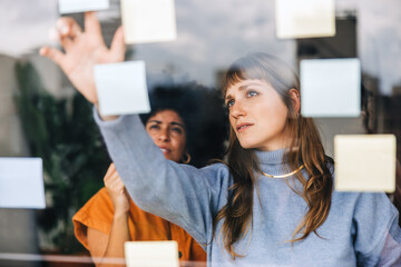 Two young businesswomen brainstorming using adhesive notes in an office