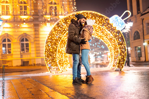 Couple hugging on city square with Christmas lights all around