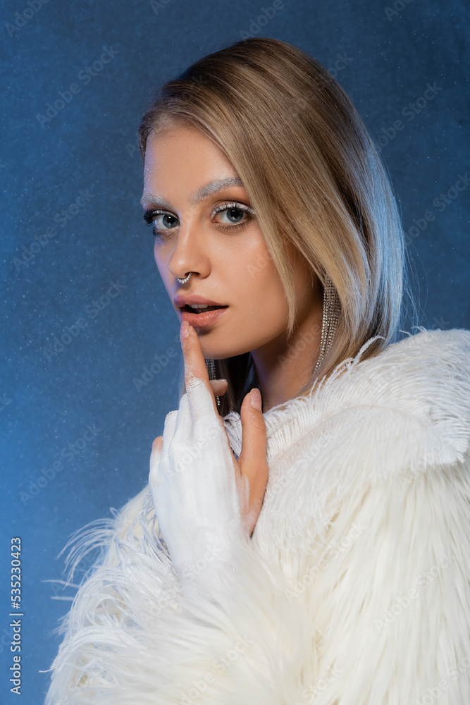 blonde woman with winter makeup and frozen eyebrows touching lip on dark blue.