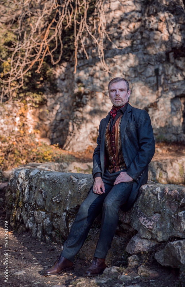 Fototapeta premium Vampire man wearing victorian suit in the autumn forest. Vintage medieval concept style.