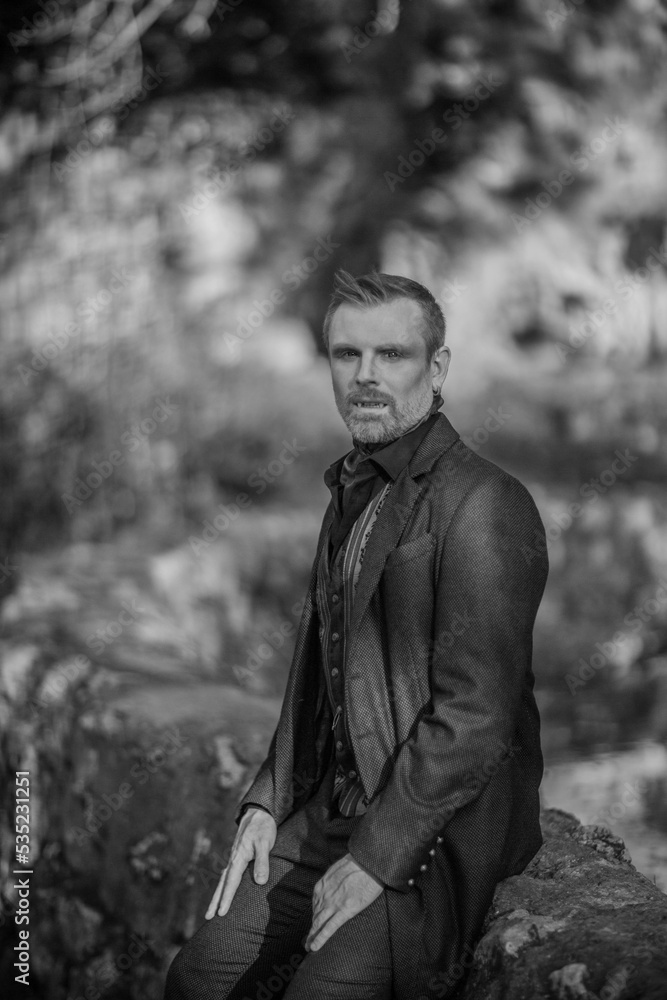 Vampire man wearing victorian suit in the autumn forest. Vintage medieval concept style. Black and white photo.
