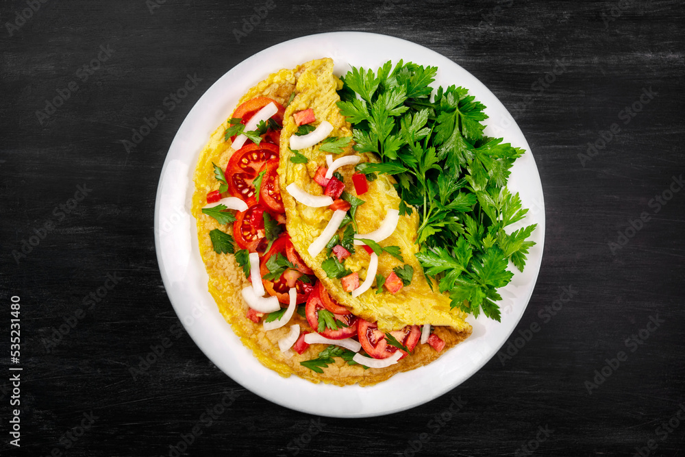 Omelet with parsley and tomatoes in a pan on a black background, top view Omelet with parsley and tomatoes in a pan on a black background, top view