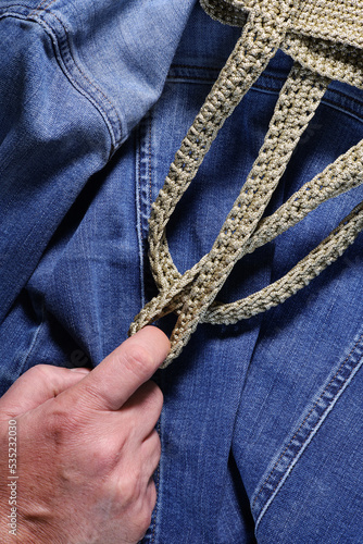 a man's hand holding the strings of a bag. Jean background