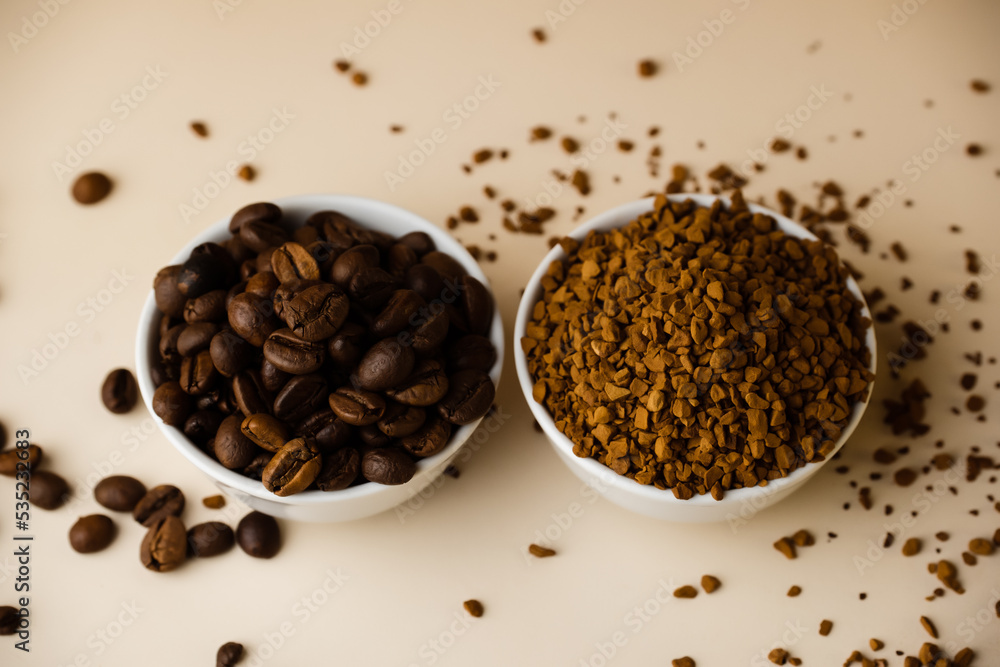 Two small bowls filled with coffee beans and instant coffee on a light table, beige background. Two small bowls filled with coffee beans and instant coffee on a light table, beige background.