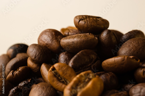 A bunch of coffee beans on a beige background. Side view, macro. © Yuliya