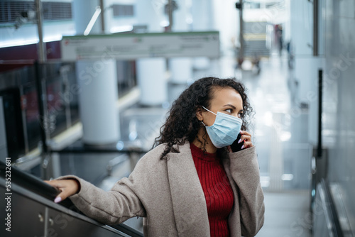 woman in a protective mask talking on a smartphone on the steps of a subway escalator.