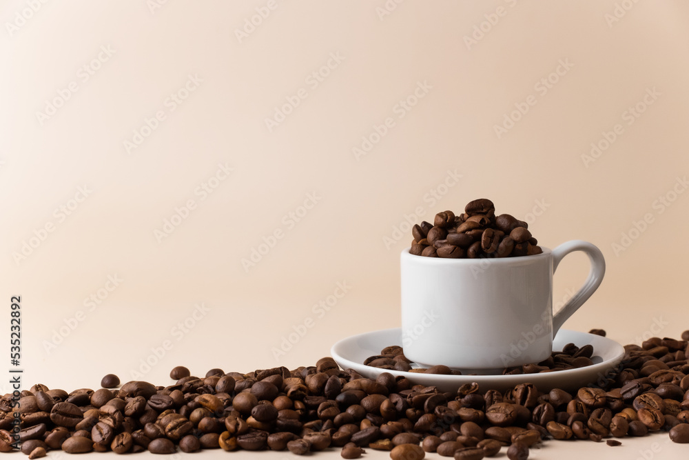 Espresso cup filled with coffee beans surrounded by a large number of coffee beans on a light beige background close-up. Espresso cup filled with coffee beans surrounded by a large number of coffee beans on a light beige background close-up.