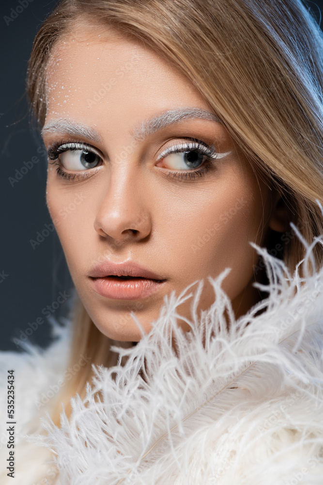 portrait of pretty young woman looking away while posing near white feather isolated on blue.