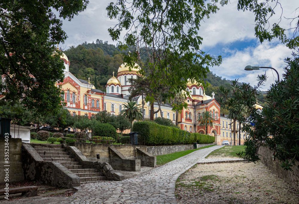 New Athos, Abkhazia - October 20, 2021. The New Athos Monastery with bright golden domes on a sunny autumn day among green trees .